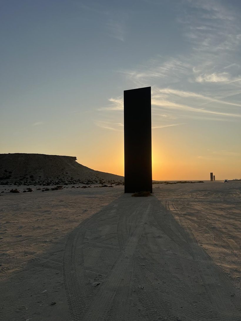 A steel monolith standing alone in open desert at sunset